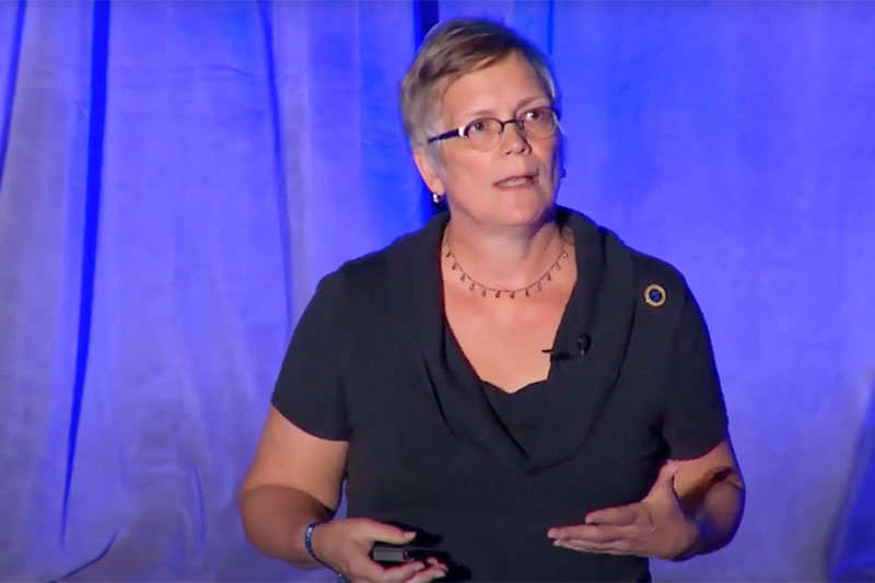 woman on stage speaking wearing glasses with short hair