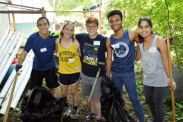 five volunteers smiling for photo while doing yard work