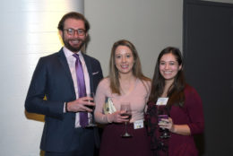 two women and a man smiling with glasses of wine in hand for photo