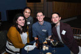 two men and two women smiling for photo in front of table of food and drink