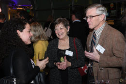 two women and a man speaking at event with glasses of wine in hand