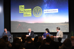 three men and a woman on stage speaking at an event