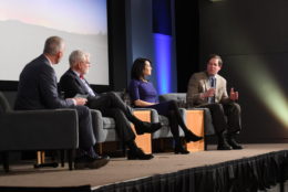 three men and a woman on stage speaking at an event