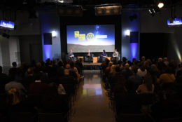 four speakers seated on stage in front of an audience