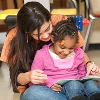 A little girl sitting on a woman's lap reading a book