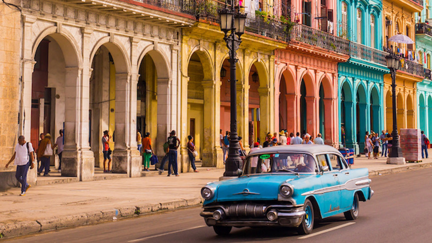 Old fashion blue car in front of a row of colorful buildings in Havana Cuba
