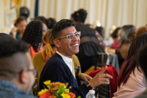 Guy with glasses sitting at in an audience smiling