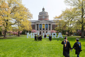 Rush Rhees library with students in graduation cap and gown on the lawn