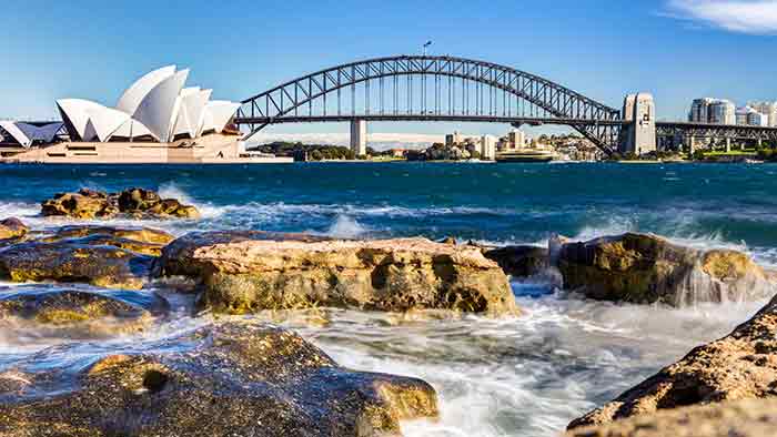 Sydney OperaHouse, with the bridge in the background with water and rocks in the foreground