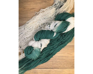 A bundle of green, white, and speckled yarn is displayed on a wooden surface, with strands laid out to show the variation in color.