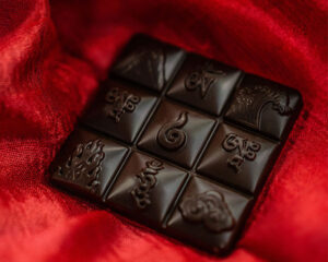 A dark chocolate square embossed with intricate symbols rests on a rich red fabric background.