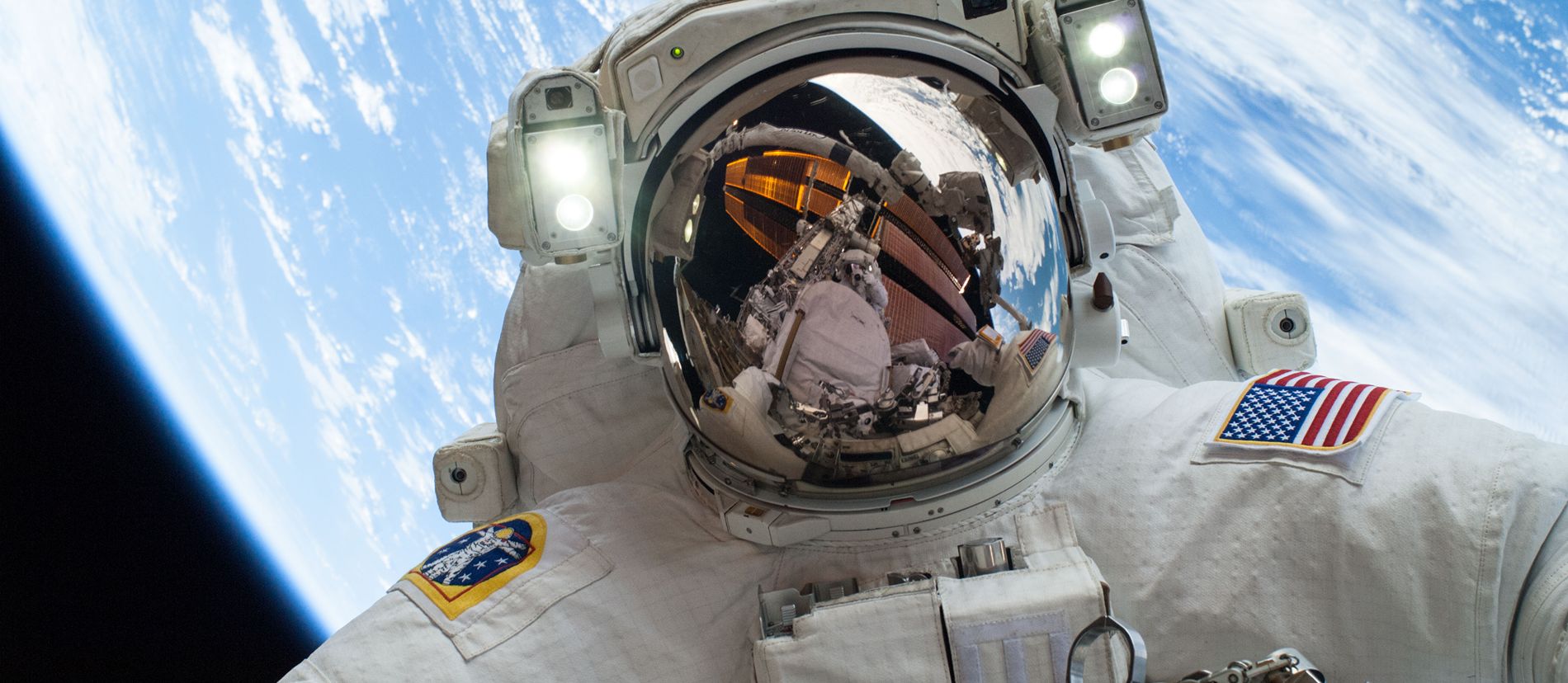 An astronaut floats above Earth during a spacewalk, with the planet’s blue atmosphere stretching across the horizon.