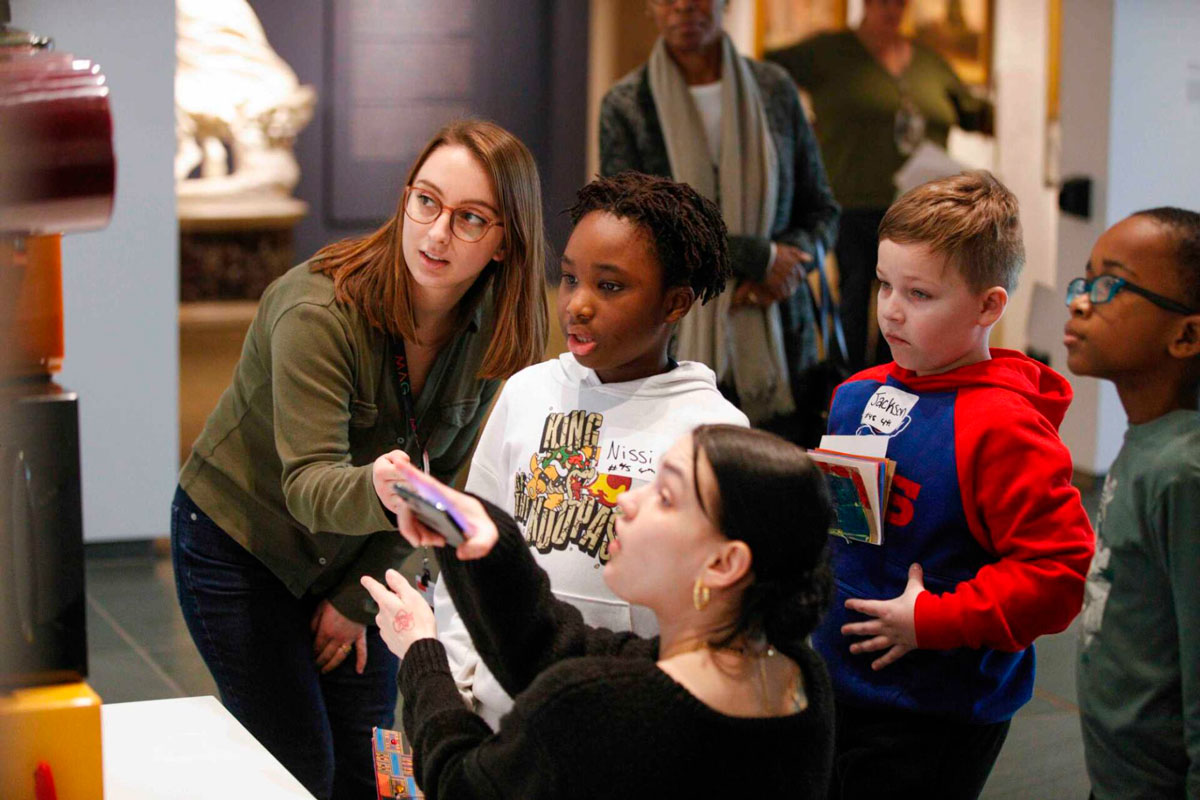 A handful of schoolchildren examine a work of art with an educator nearby.
