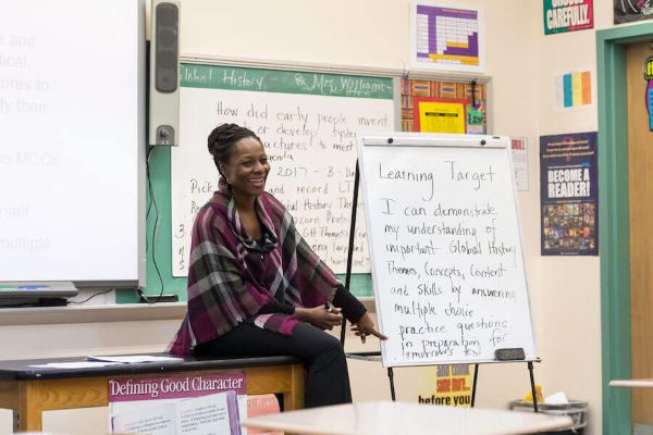 A teacher laughing at the front of a classroom, discussing learning targets with her students