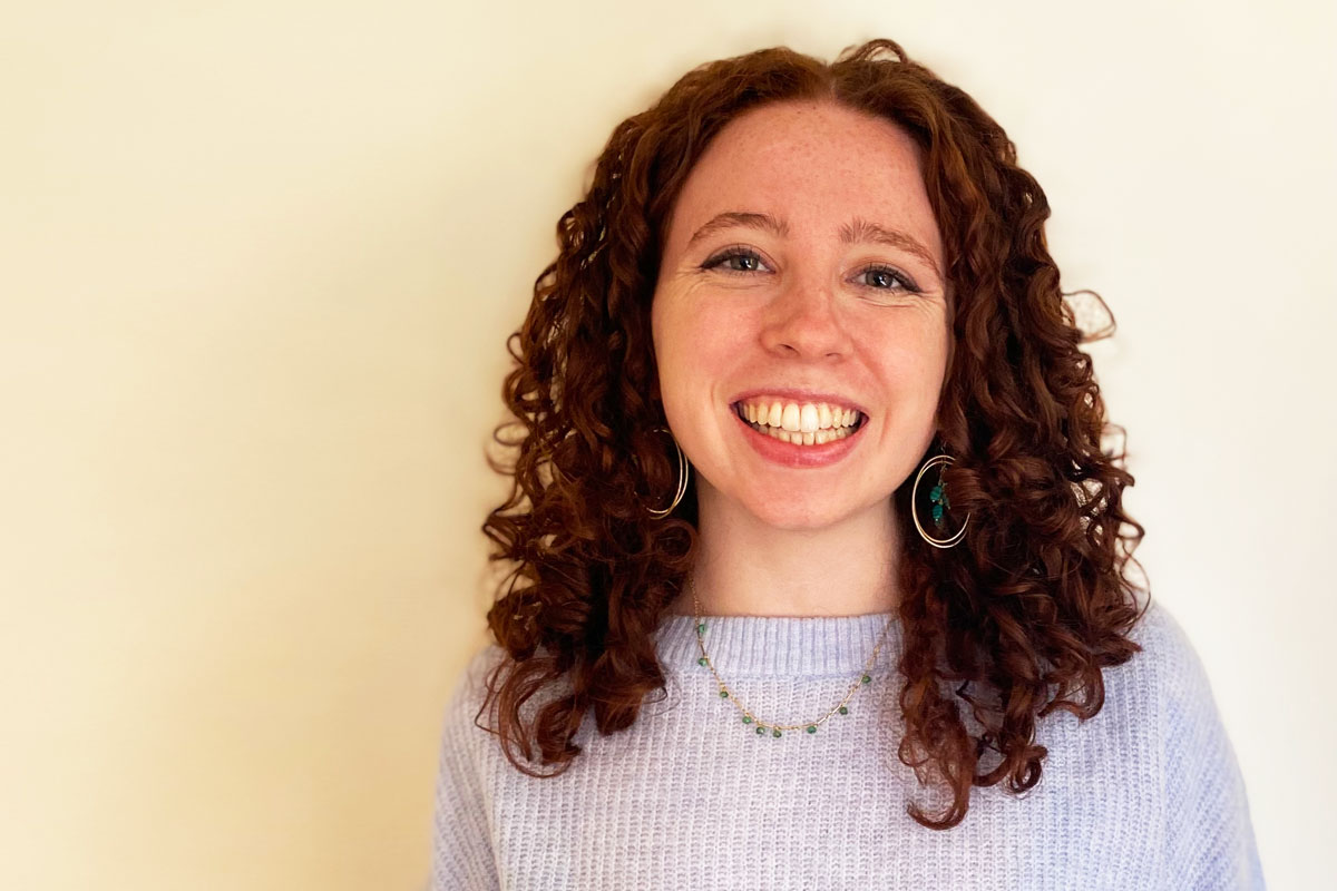 Person with curly hair smiling, wearing a purple sweater.