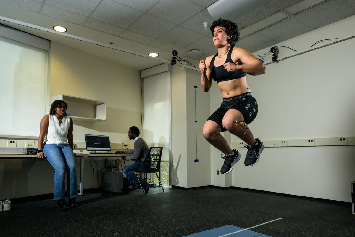 A woman leaps joyfully in a room at the University of Rochester, capturing a moment of exuberance and energy.