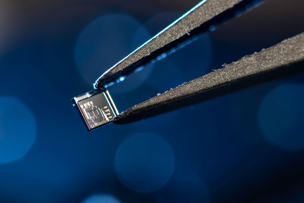 A researcher at the University of Rochester holds a small microchip with tweezers, showcasing precision in technology.