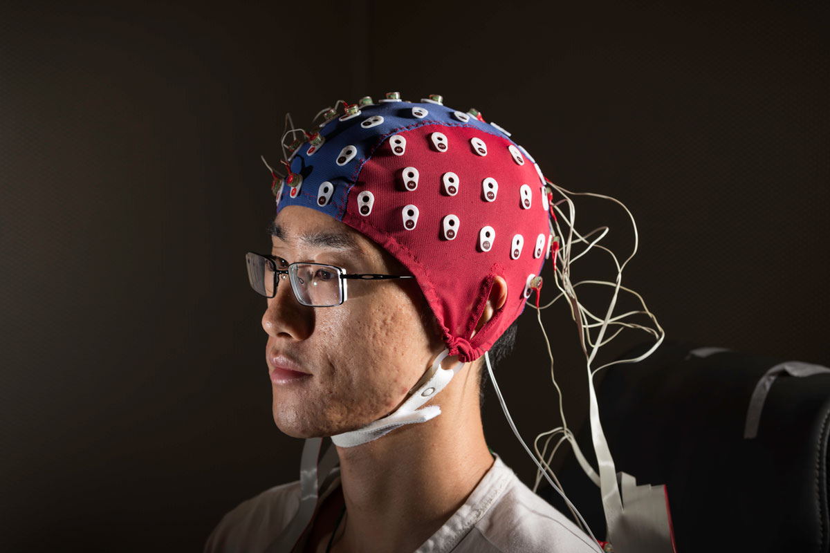 A man in an EEG cap sits in a chair at the University of Rochester, engaged in a neurological study.
