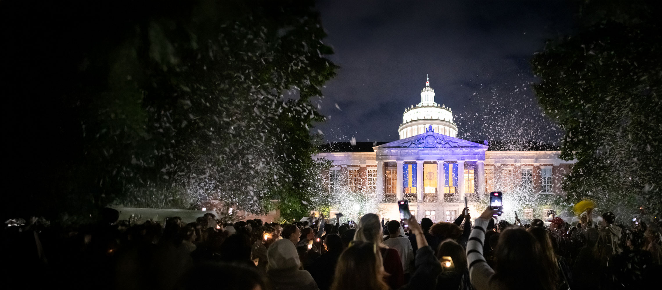 People stand in front of a University of Rochester building as water cascades from the sky, creating a serene atmosphere.