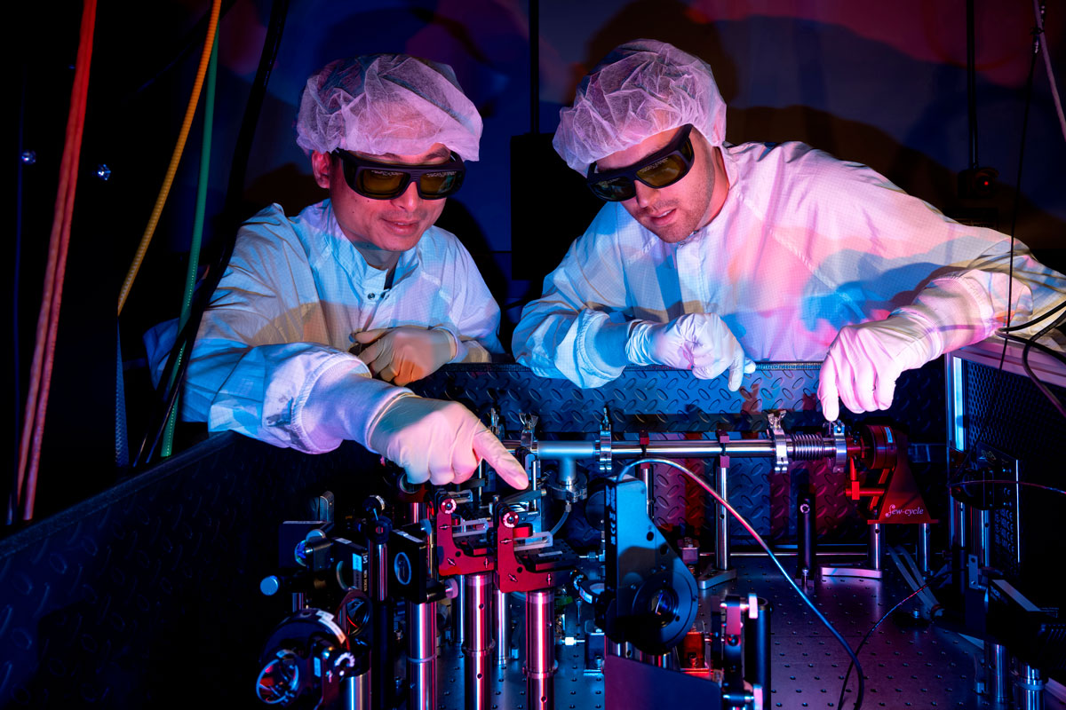Two men in white lab coats collaborate on a machine at the University of Rochester’s Laboratory for Laser Energetics.