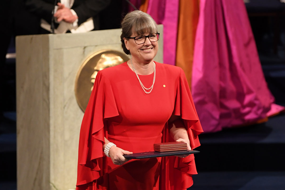 A woman in a red dress proudly holds a plaque, showcasing her achievement with a confident smile.
