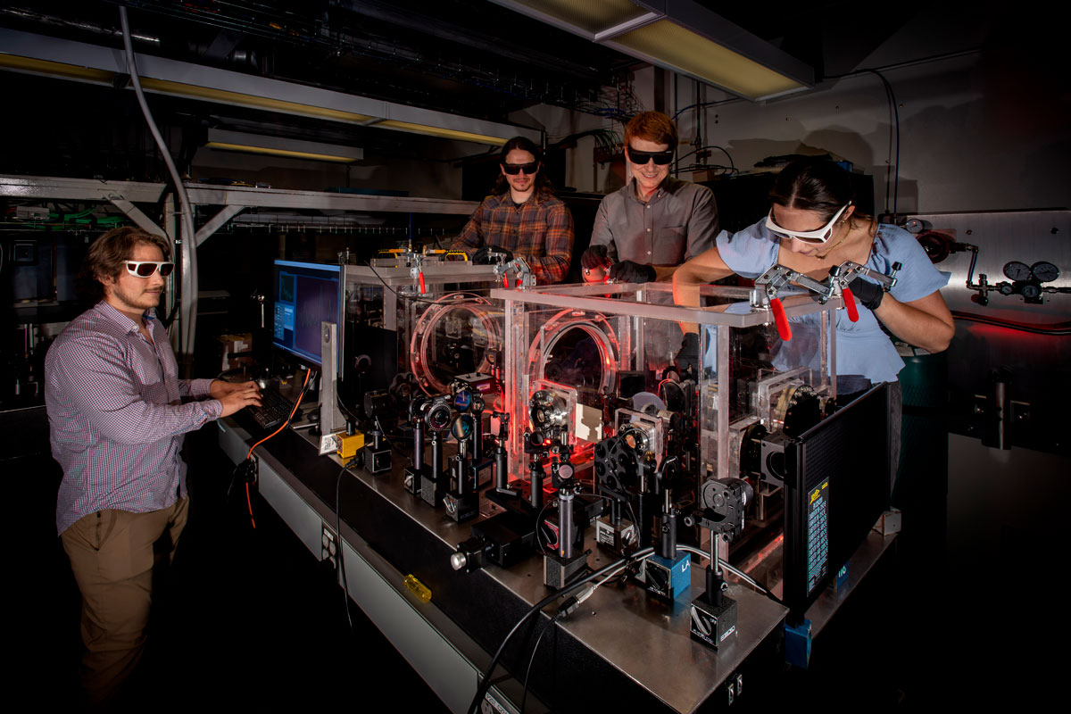 Three men collaborate in a lab at the University of Rochester’s Laboratory for Laser Energetics, surrounded by equipment and computers.
