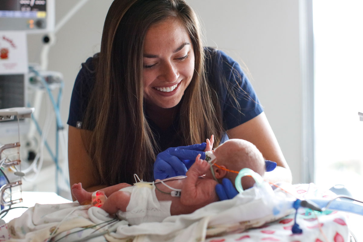 A nurse gently holds a baby in an incubator at the University of Rochester health care facility, showcasing compassionate care.
