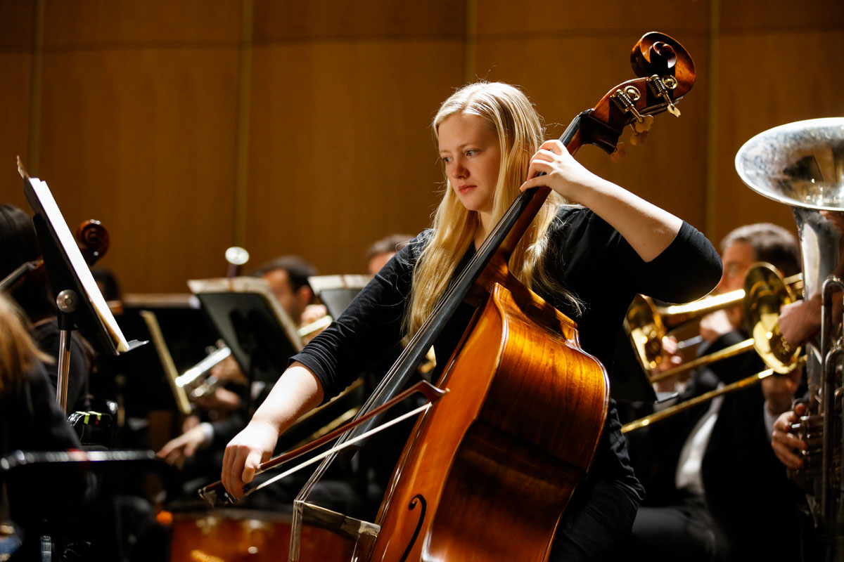 A woman performs on the cello within an orchestra at the University of Rochester's Eastman School of Music.