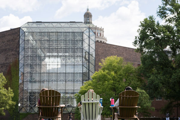 A young adult poses for a photo in front of the University of Rochester's Rush Rhees Library.