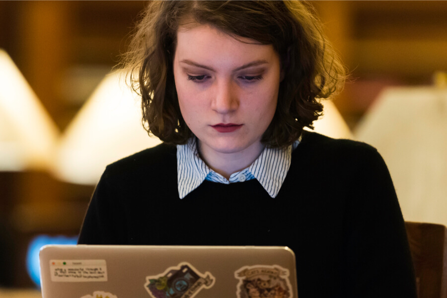 A young woman at a table with a laptop, studying at the University of Rochester.