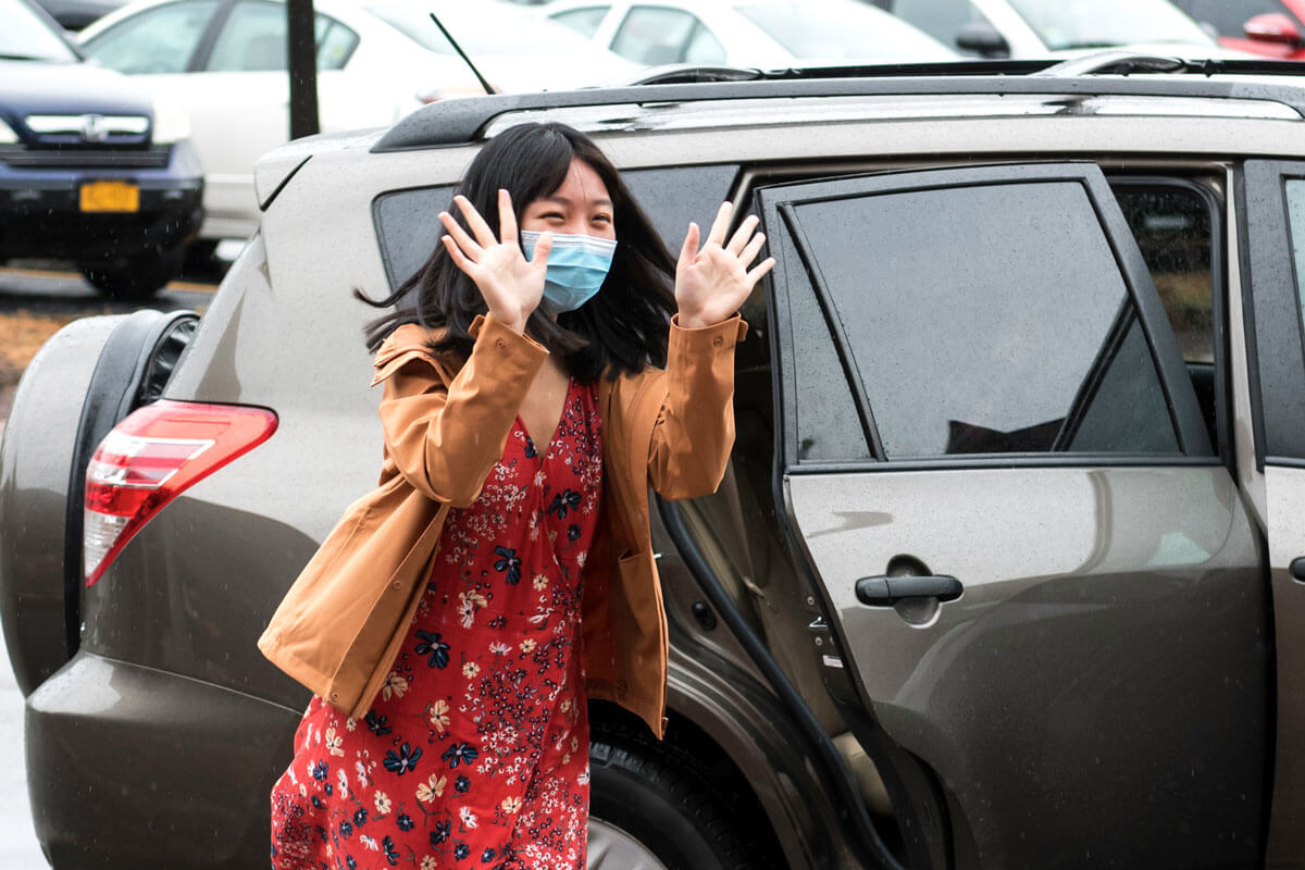 A masked University of Rochester student moving onto campus, smiling and waving.