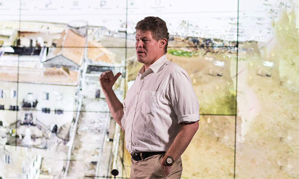 A photo of Michael Jarvis in front of a large screen with a map of Brmuda.
