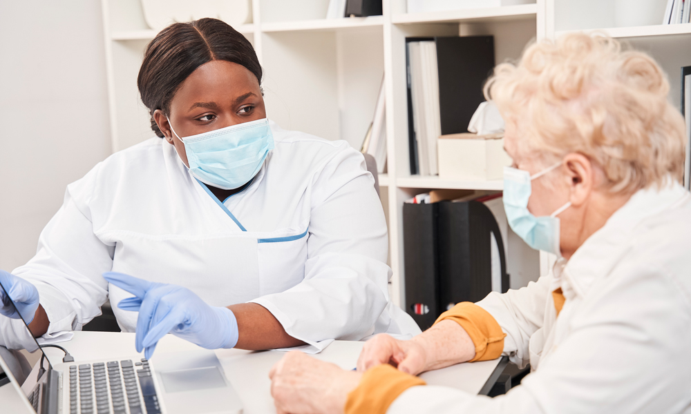 A woman in medical mask and gloves talking to an older woman in a caring and compassionate manner.