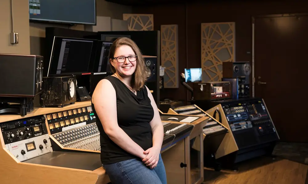 Grace Stensland smiles while leaning against a sound mixing console.