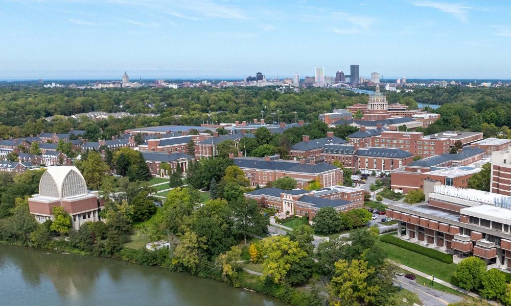 Aerial view of the University of Rochester campus with the city of Rochester's skyline in the background on a clear, sunny day.