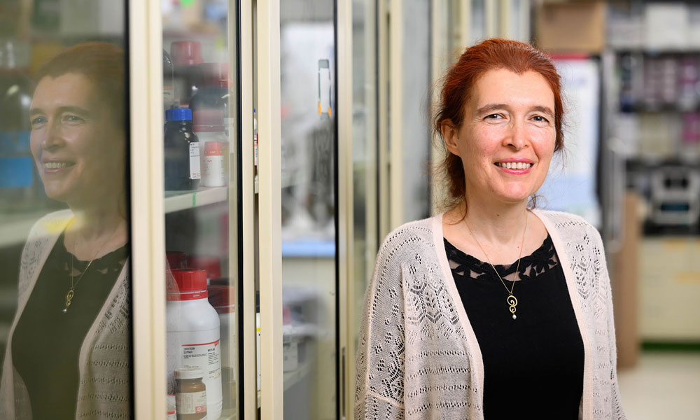 Vera Gorbunova smiles at the camera with her reflection in the cases of her lab.