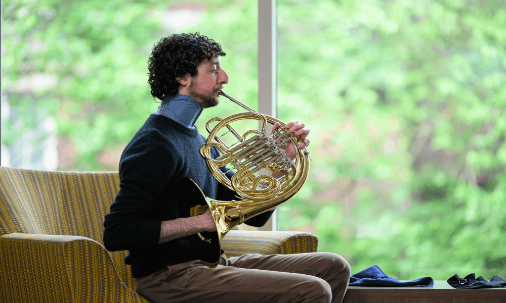 A man plays the french horn while wearing a custom neck brace