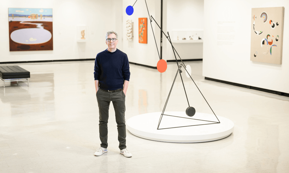 Timothy Peterson stands with his hands in his pockets in the Memorial Art Gallery surrounded by several art pieces
