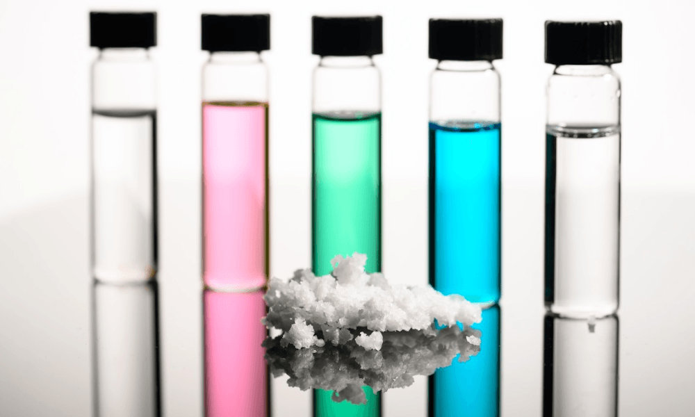 A series of vials containing different colors of liquid stand in the background of a small pile of salt