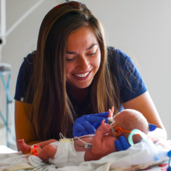 A smiling woman holds a baby in a hospital bed at the University of Rochester, radiating joy and tenderness.