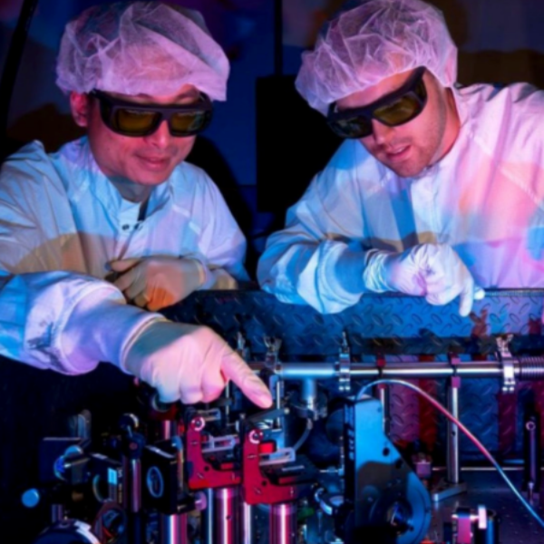 Two men in white lab coats operate a machine at the University of Rochester's research facility.
