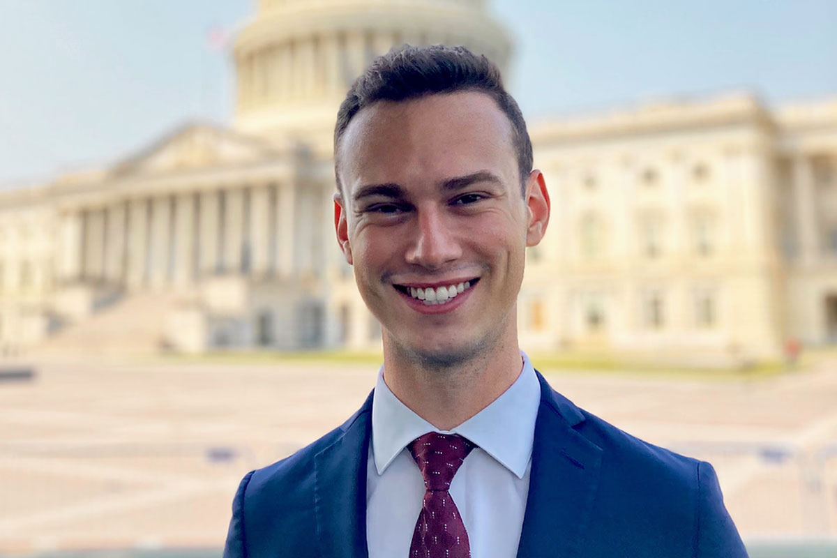  smiling man in a suit and tie stands in front of the Capitol building, representing University of Rochester alumni.