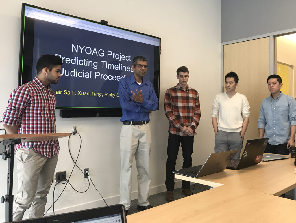 Three Students and a professor in front of a presentation screen