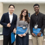 Three students in professional attire, pose for a photo holding their showcase packets