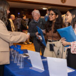 Showcase attendees having a conversation in front of a sponsor table picking up swag during the poster session.