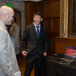 A student is sharing their research technology with a man in business attire during the poster session.