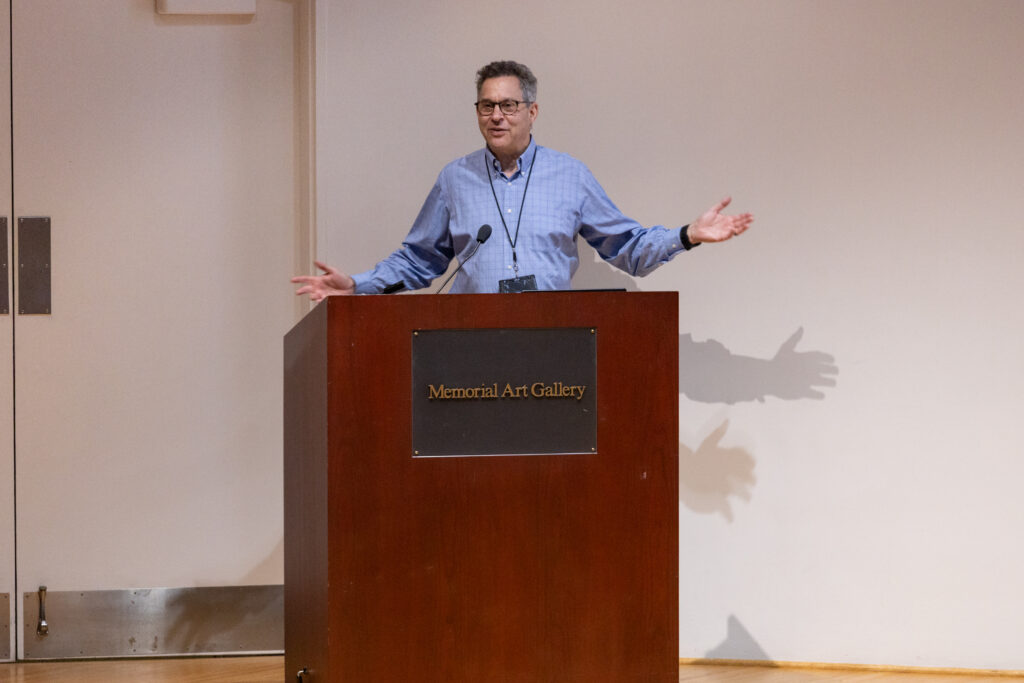 Barry Silverstein at podium on stage smiling with his arms open as he delivers his keynote.