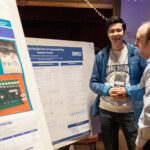 A male student shares there work with another attendee who is viewing thei poster on Flux Bias Driver for Superconducting Quantum Circuits.