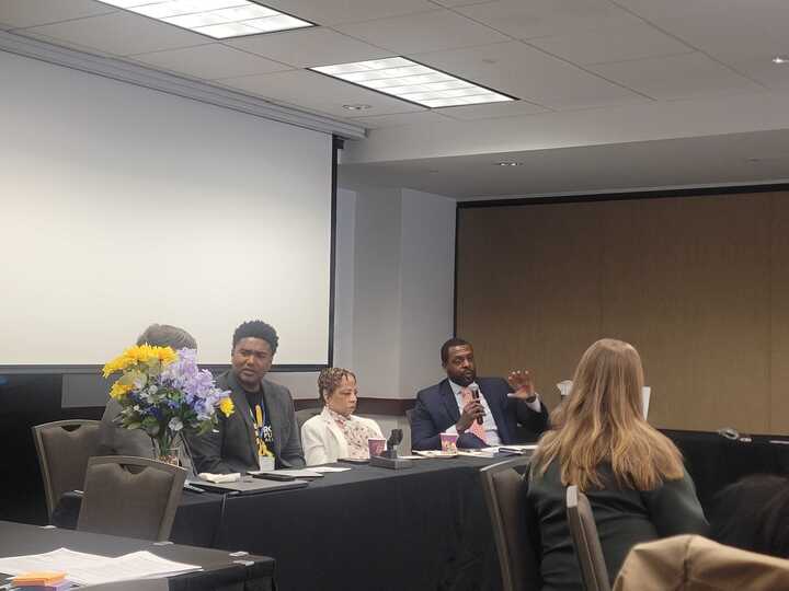 A panel member speaks from behind a table.