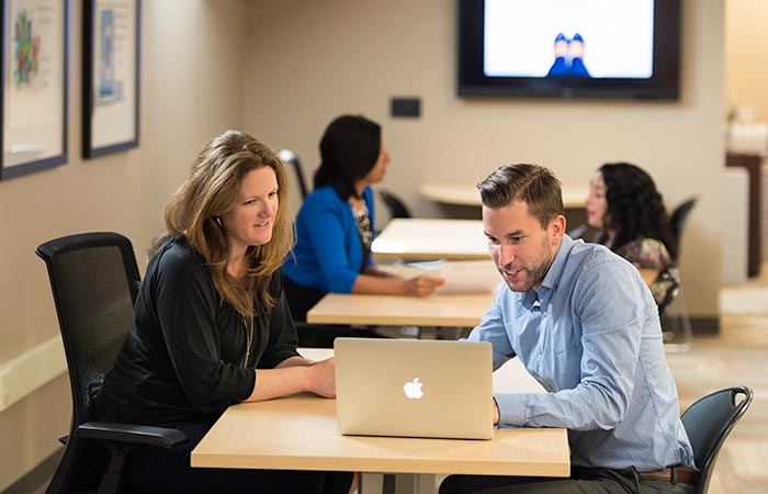 A man and a woman meeting at a table and looking at a computer.